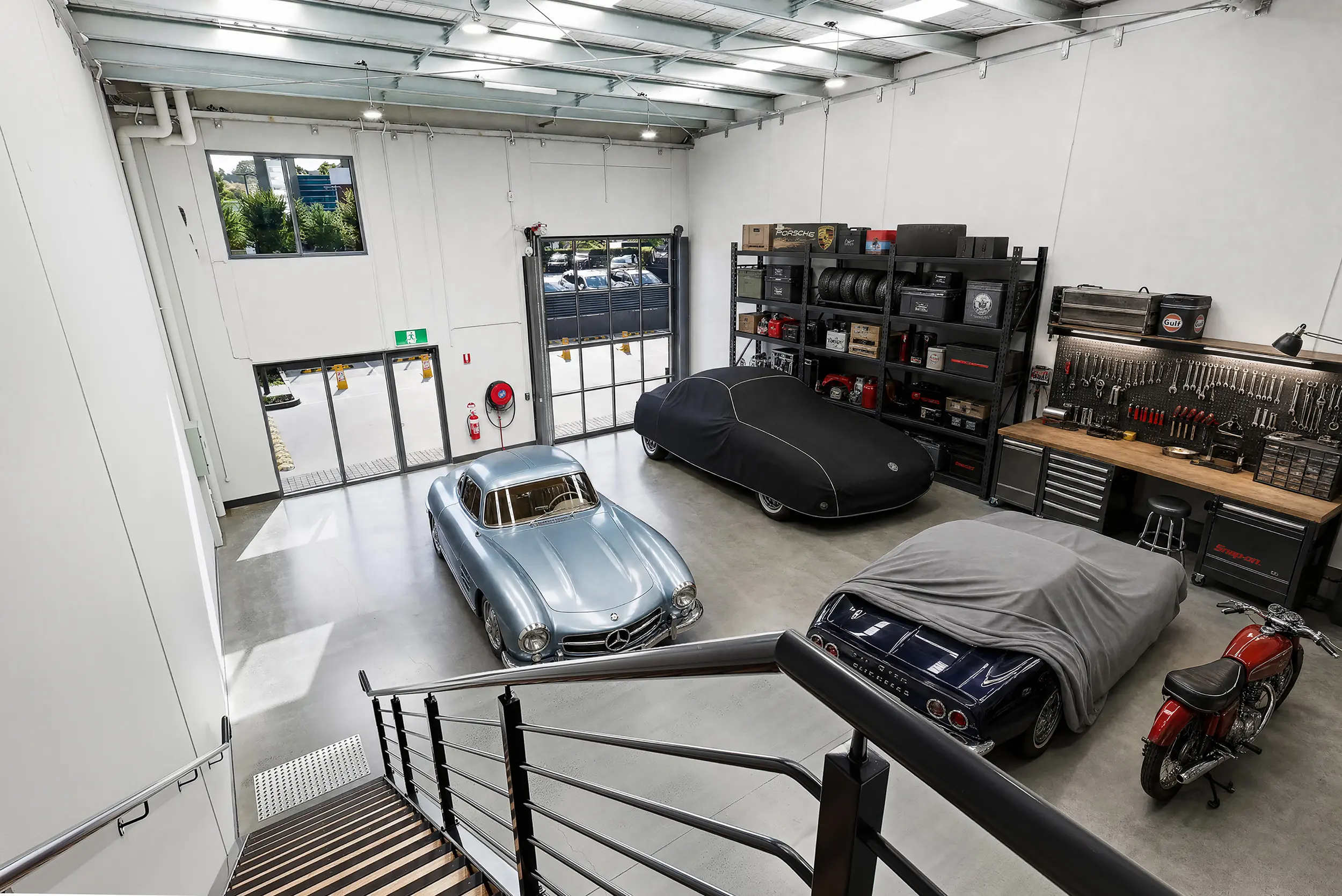 A Jacoah Place tenancy styled as a private classic car garage, with a Mercedes gullwing, covered cars and a fitted workbench under the high-clearance roof
